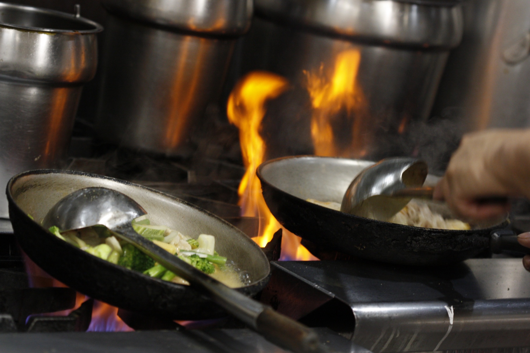 Two pans searing over a fiery burner